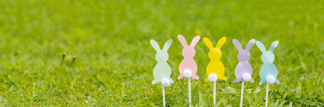 On a light blue background, Easter bunnies cut out of colored paper, scissors, felt-tip pens. Easter holiday concept, children's crafts, applique. Flat lay, top view, pattern.