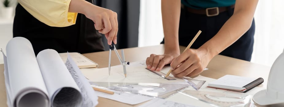 Professional architect team used divider measure during draft blueprint on table with architectural document, safety helmet and blueprint scatter around. Closeup. Focus on hand. Delineation.