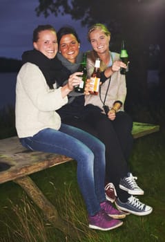 Friends, portrait and beer outdoor at night for camping adventure, nature celebration or group connection. Woman, face and smile for alcohol drinking or cheers toast for summer, travel or vacation.