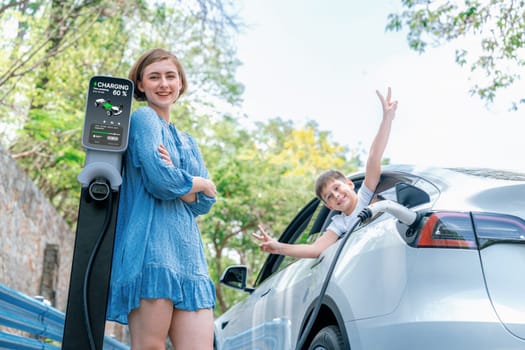 Family road trip vacation with electric vehicle, mother and son recharge EV car with green and clean energy. Nature and travel with eco-friendly car for sustainable environment. Perpetual