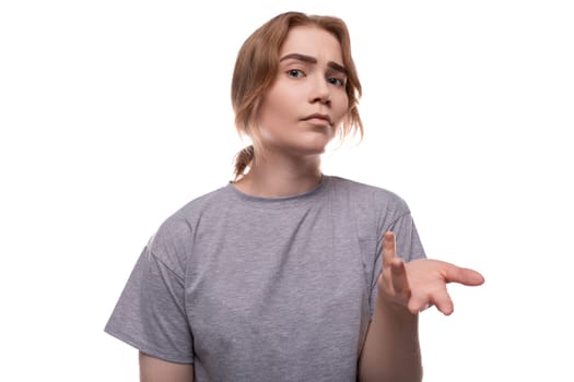 Caucasian fair-haired teenage girl in a gray T-shirt points with her hand at the camera.