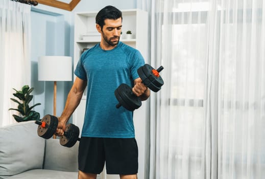 Athletic body and active sporty man lifting dumbbell weight for effective targeting muscle gain at gaiety home as concept of healthy fit body home workout lifestyle.