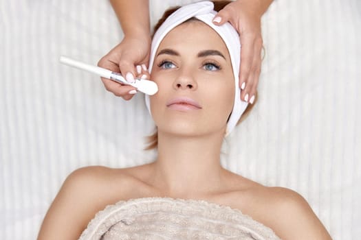 female hand touching the patient's face with a brush. beautician applies the mask to female face. facial skin care. top view