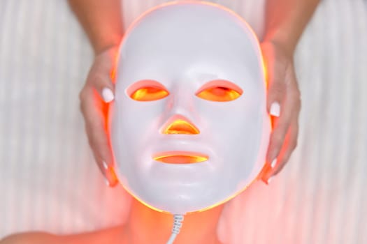 woman getting cosmetic procedure with LED anti-aging facial mask in beauty salon