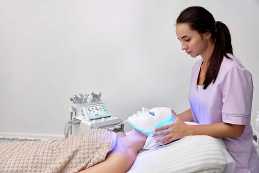 woman getting cosmetic procedure with LED facial mask in beauty salon