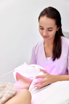 woman receiving led light therapy mask treatment from beautician in beauty salon