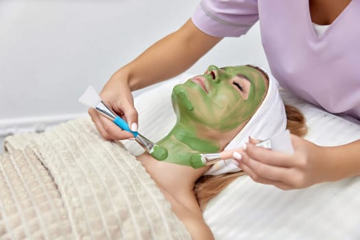 female beautician applies the mask to the face of beautiful woman in the spa salon. facial skin care