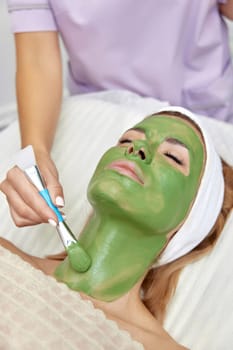 female beautician applies the mask to the face of beautiful woman in the spa salon. facial skin care
