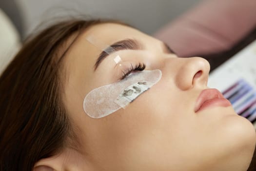 Beautiful female face during lash extension procedure in salon. Fake eyelashes