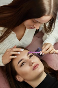 master combs the eyelashes of the client after the eyelash extension procedure. Cosmetology and skin care