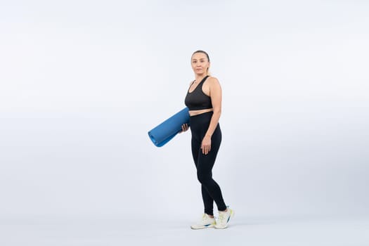 Full body length shot athletic and sporty senior woman holding fitness exercising mat on isolated background. Healthy active physique and body care lifestyle after retirement. Clout