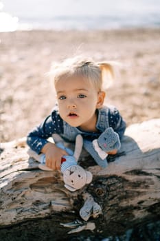 Little girl leaned her stomach against a snag with soft toys in her hands. High quality photo