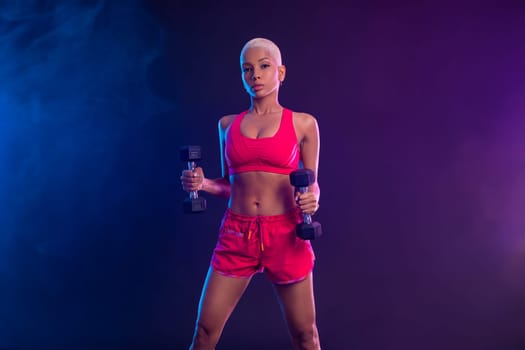 Sporty fit woman, athlete with dumbbells make fitness exercises on black background. Download cover for music collection for fitness classes. Sports recreation. Beautiful black young woman