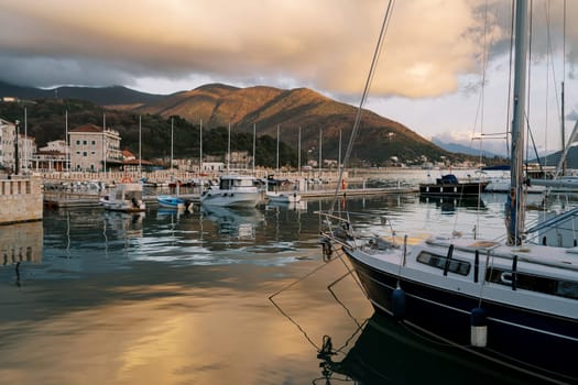 Row of yachts stands at the pier of the resort town at the foot of the mountains in the reflections of the setting sun. High quality photo