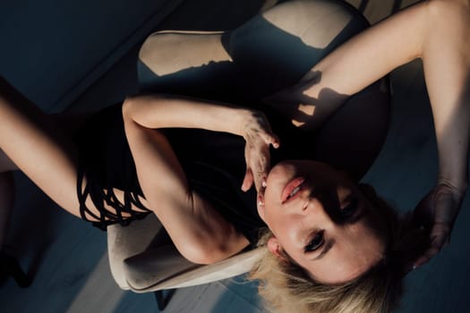 Beautiful blonde woman on armchair in black bodycon evening dress