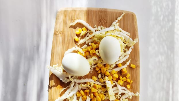 Chopped Peking cabbage, peeled eggs and yellow canned corn on cutting board as background. Cooking a healthy eco-friendly salad from natural products. Copy space and place for text