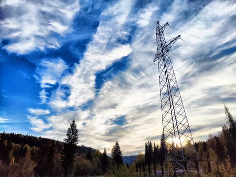 Power lines on a hill, hill or in the mountains against a blue sky with white clouds. Electric lines, towers, wires in nature landscape