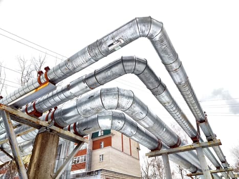 Metal pipes in thermal insulation winding outdoors and the over-illuminated white sky on background