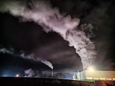 Winter night industrial landscape. Coal-fired power station with smoking chimneys against dramatic dark sky. Carbon dioxide CO2 emissions as primary driver of global climate change. Air pollution