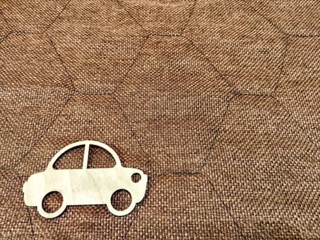 Small wooden toy on background of brown burlap fabric with embroidered diamonds. Concept of buying or traveling by car. Abstract texture, pattern, place for text, copy space. Partial focus, blurred