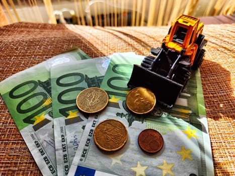 A small toy tractor or excavator on bundle of money. The concept of the high cost of technology. The possibility of earning money with construction machinery