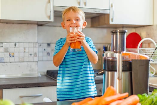 Little boy drinking freshly squeezed carrot juice from a glass in the kitchen. Concept of healthy and delicious food