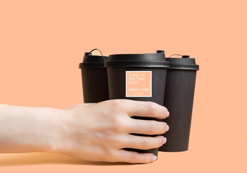 Peach fuzz, color of the year, 2024. Woman hand holding one black take away coffe cup on neutral pastel background