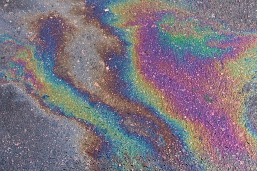 Colored texture of oil products on the asphalt in the rain. Oil dripped from the car engine onto the road.