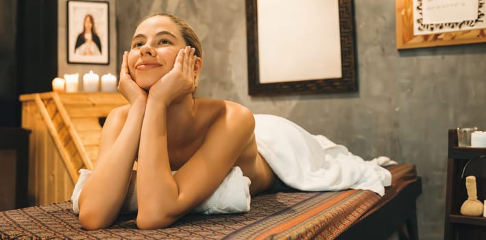 Portrait of beautiful caucasian woman in white towel woman lies on spa bed in front of warm wooden sauna cabinet with relaxation and peaceful at spa salon. Close up. A Side view. Tranquility.