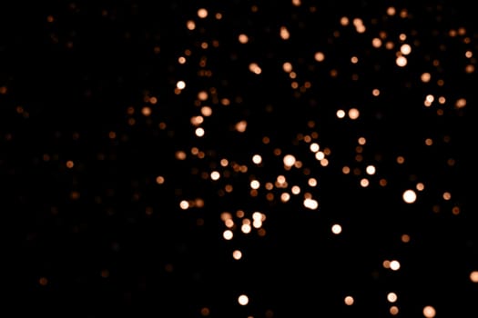 Blurry garland lights on a dark background. Festive Christmas and New Year background. Soft focus. Image toned in color of the year 2024 - Peach Fuzz.