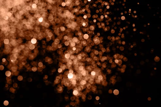 Blurry garland lights on a dark background. Festive Christmas and New Year background. Soft focus. Image toned in color of the year 2024 - Peach Fuzz.