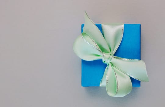 Gift box tied with satin pale green ribbon on a light gray paper background. copy space, place for text,