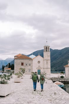 Couple walk holding hands towards the Church of Our Lady of the Rocks. Back view. Montenegro. High quality photo