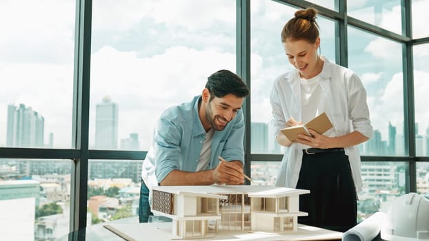 Skilled architect engineer team discussion about house model construction. Smart interior designer sharing, talking about building design while beautiful coworker taking a note. Design. Tracery