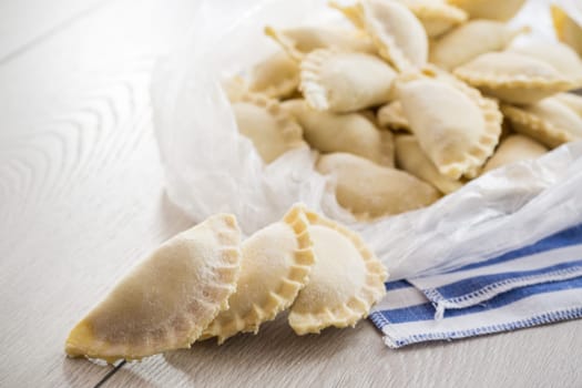 Raw dumplings with filling inside, Ukrainian cuisine. Raw dumplings for freezing in a bag on a light wooden table. Home kitchen.