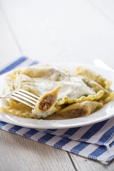 cooked dumplings with meat, spices and sour cream, in a plate on a light wooden table. Ukrainian food.