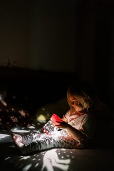 Little girl sits on a bed with a projector night light in her hands and looks at it. High quality photo