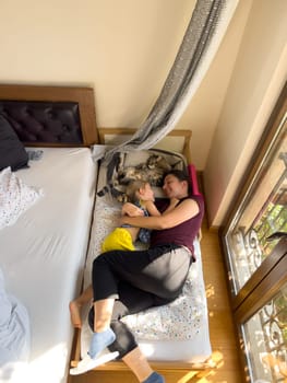 Mom and little girl lie hugging on a children bed near a cat. High quality photo