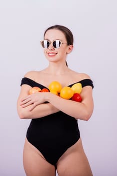 Smiling cool girl in a sun glasses in black swimsuit posing with fruits and laughing.