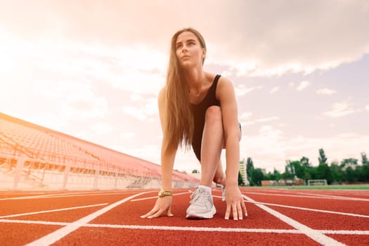 A female coach with dark hair stands on the red running track of the stadium, dressed in sports uniform.