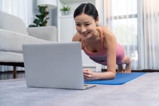 Fit young asian woman planing on the living room floor while following exercise instruction on online training video. Healthy lifestyle workout routine at home. Balance and endurance concept. Vigorous