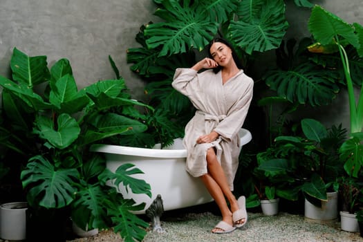 Tropical and exotic spa garden with bathtub in modern hotel or resort with young woman in bathrobe enjoying leisure and wellness lifestyle surrounded by lush greenery foliage background. Blithe