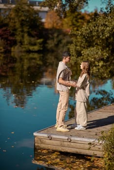 A happy couple in love in casual clothes travel together, hike and have fun in the fall forest on a weekend in nature in autumn outdoors, selective focus. Handsome man embracing with passion his girlfriend outdoor under the leaves of trees on the embankment. Love history. Happy people concept