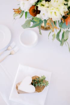 Invitation succulent in a pot with a paper heart on a set table with a bouquet of flowers. High quality photo
