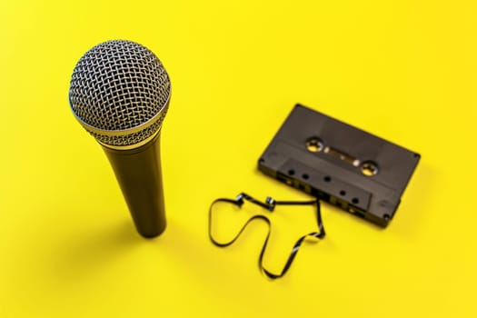 Microphone and audio cassette with some magnetic tape out, on yellow board.