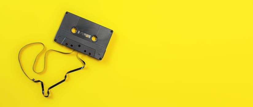 Overhead shot - magnetic audio cassette with some tape out, on yellow board, wide banner space for text on right side.