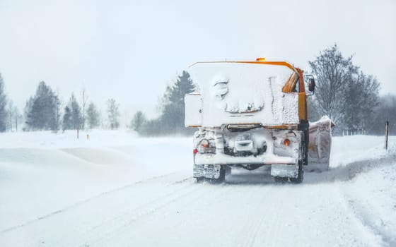 Snow plow gritter maintenance truck on winter road, completely white after heavy blizzard, view from rear