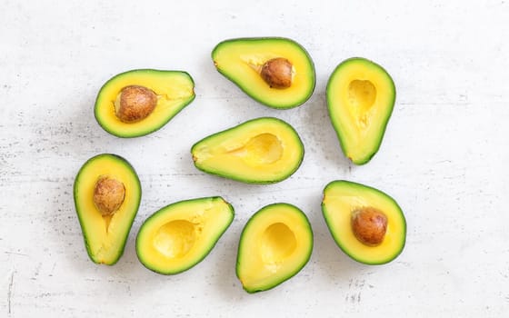 Avocado halves, some with seeds on white board, flat lay view