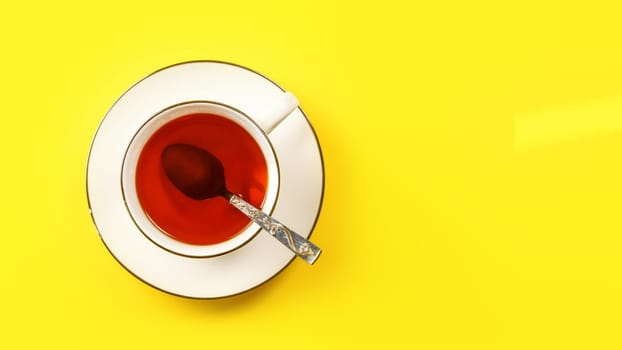 Flat lay photo, white porcelain cup of hot tea with silver spoon, on yellow board, space for text right