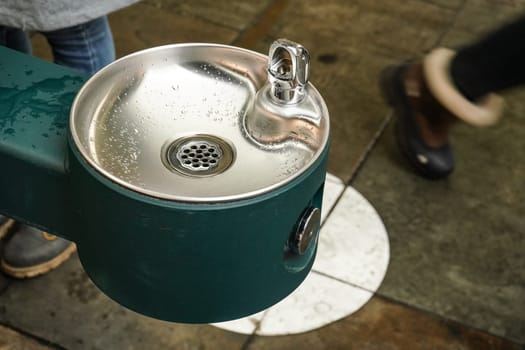 Clean stainless steel drinking water fountain on the street, blurred feet of people in background